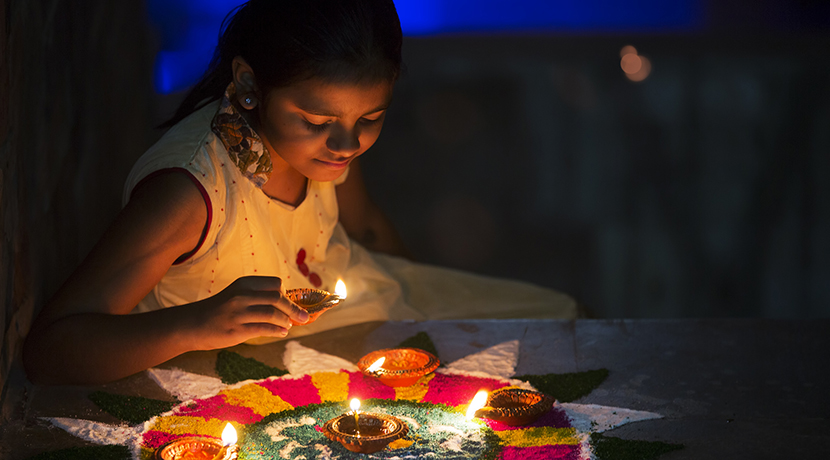 Girl making Rangoli and decorating with Oil lamps for Diwali